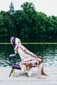 woman in white hijab sitting on black and pink chair near body of water during daytime